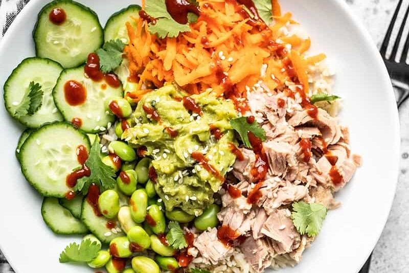 Overhead view of a Spicy Tuna Guacamole Bowl with sriracha and sesame seeds sprinkled over top.