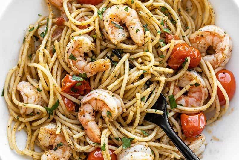 Overhead view of a bowl full of pesto shrimp pasta with a black fork in the middle