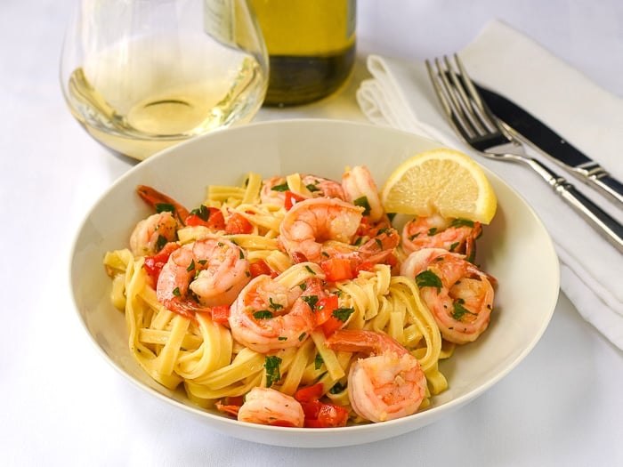 Super Simple Shrimp Scampi wide shot photo of a single serving in a white bowl with wine in background