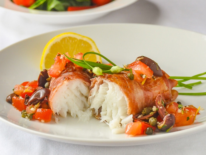 Prosciutto wrapped cod with lemon and salsa on a white plate