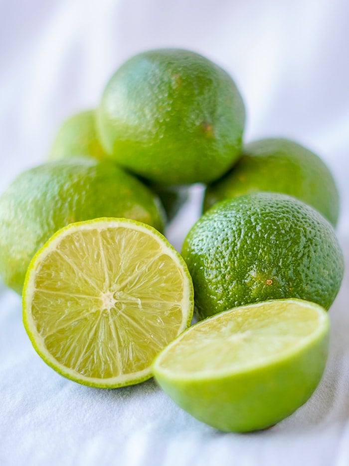 photo of limes on a white background with one cut to reveal the interior.