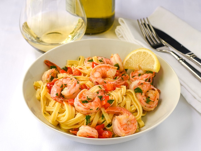 Super Simple Shrimp Scampi wide shot photo of a single serving in a white bowl with wine in background