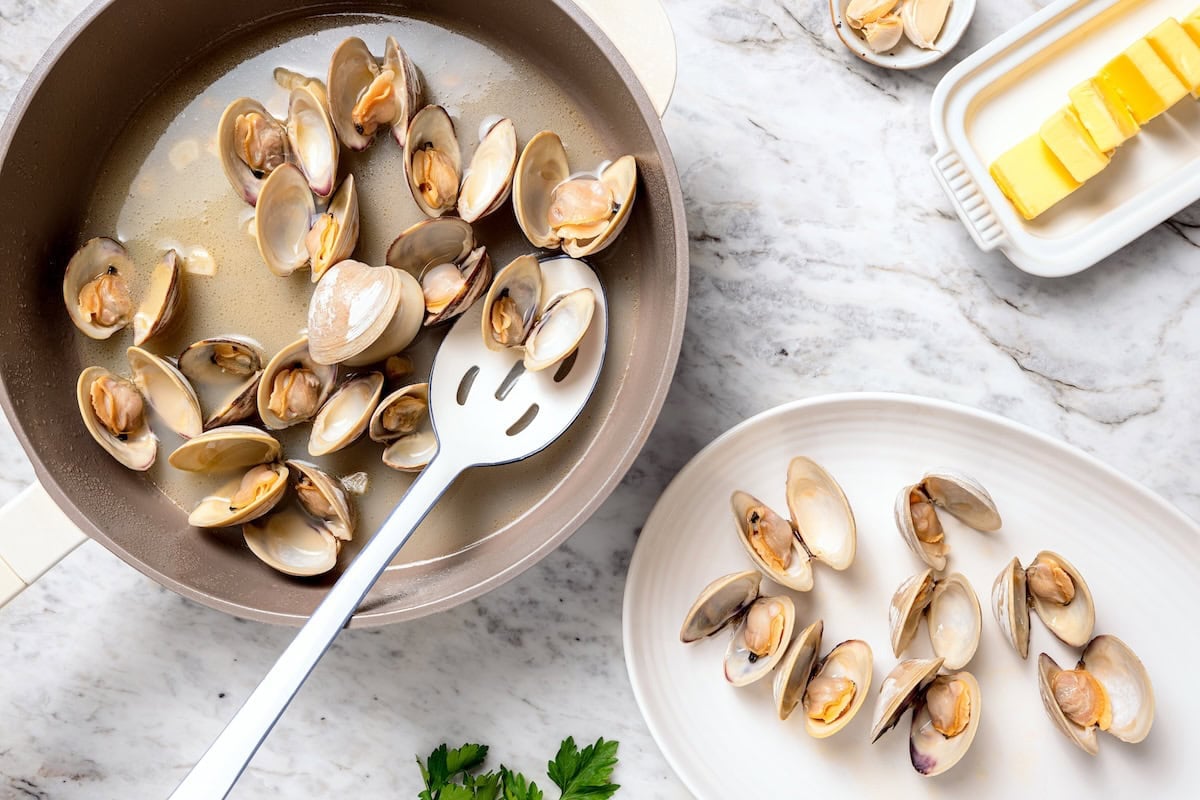 These steamed clams are flavorful and surprisingly easy. With a garlicky white wine broth, they're lighter than the restaurant version too! Slotted spoon removing steamed clams from skillet.