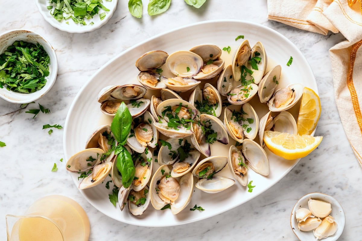 These steamed clams are flavorful and surprisingly easy. With a garlicky white wine broth, they're lighter than the restaurant version too! Platter of steamed clams with basil.