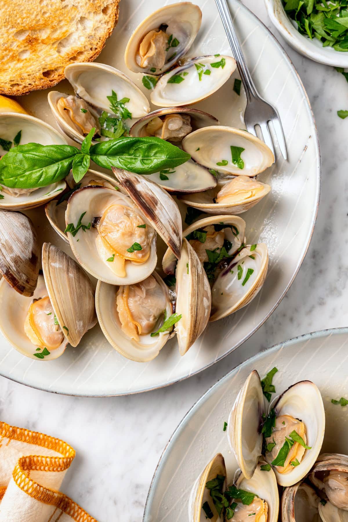 These steamed clams are flavorful and surprisingly easy. With a garlicky white wine broth, they're lighter than the restaurant version too! Steamed clams on platter with fresh basil.