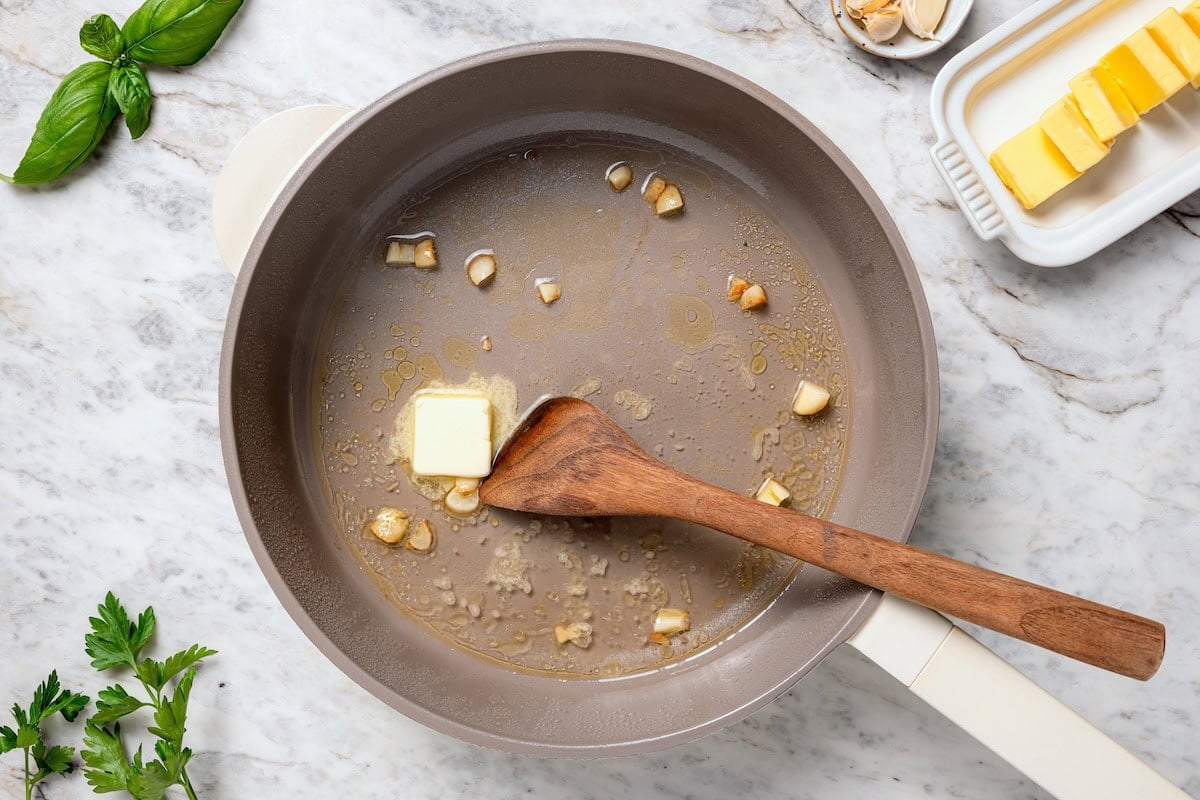 These steamed clams are flavorful and surprisingly easy. With a garlicky white wine broth, they're lighter than the restaurant version too! Butter melting in pan with wine and garlic.