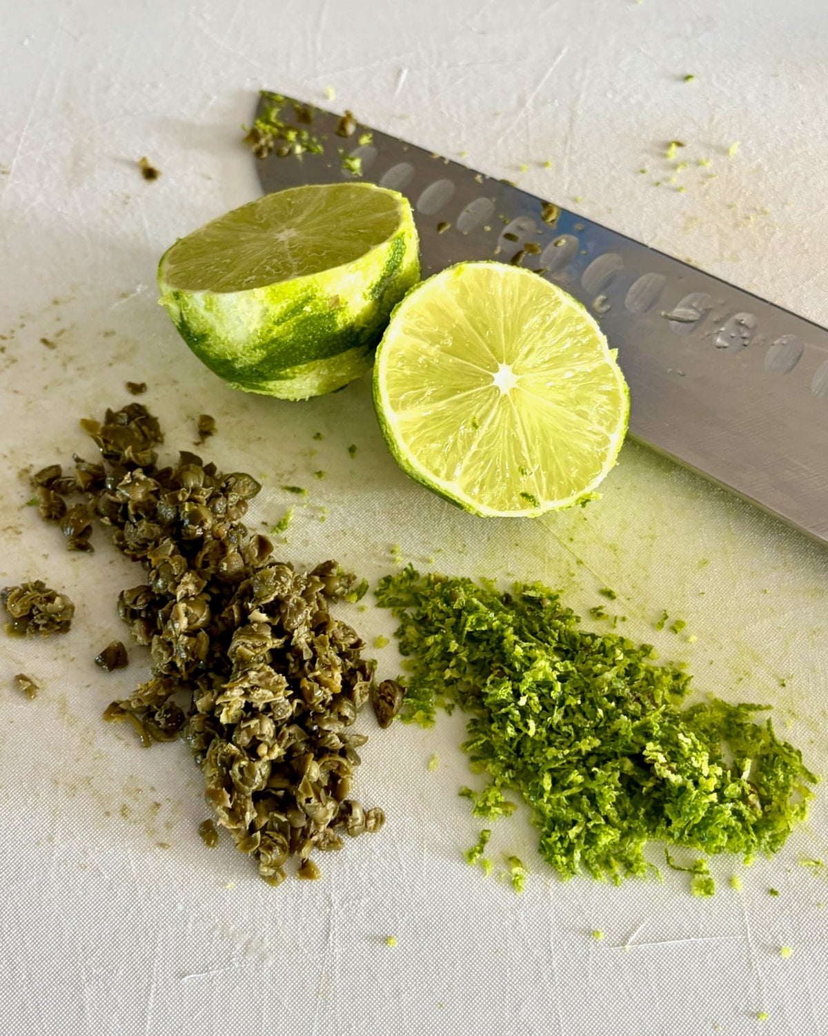 Photo of chopped capers and lime zest on a white cutting board.